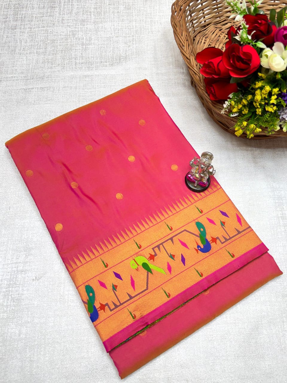 Pink and orange fabric with patterns on a white surface, next to a basket of flowers.