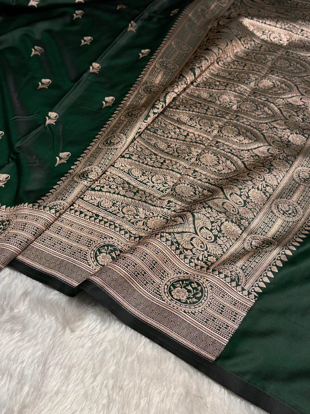 Close-up of a green saree with intricate gold patterns on a white surface