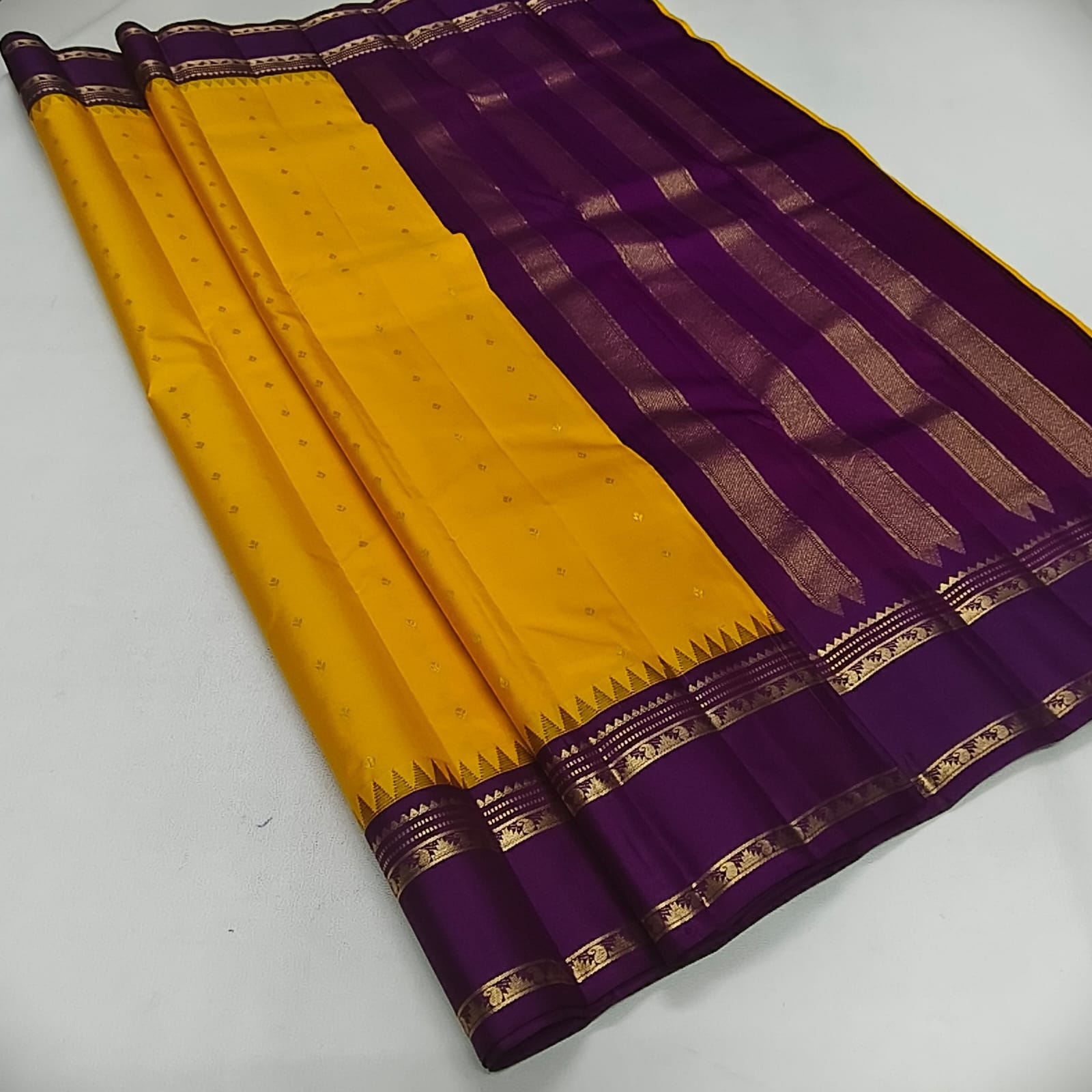 A traditional Indian silk saree with a vibrant yellow body and a deep purple border, decorated with intricate gold zari metallic patterns.