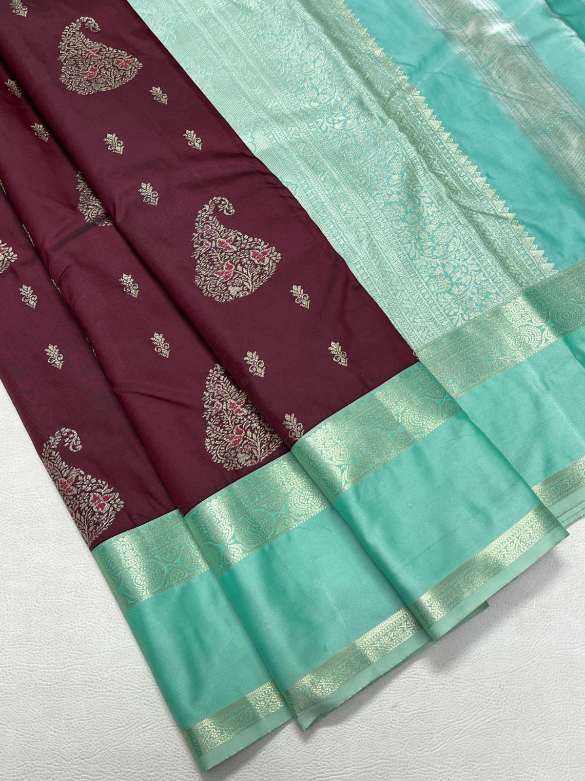 Maroon and turquoise saree with intricate patterns on a white background