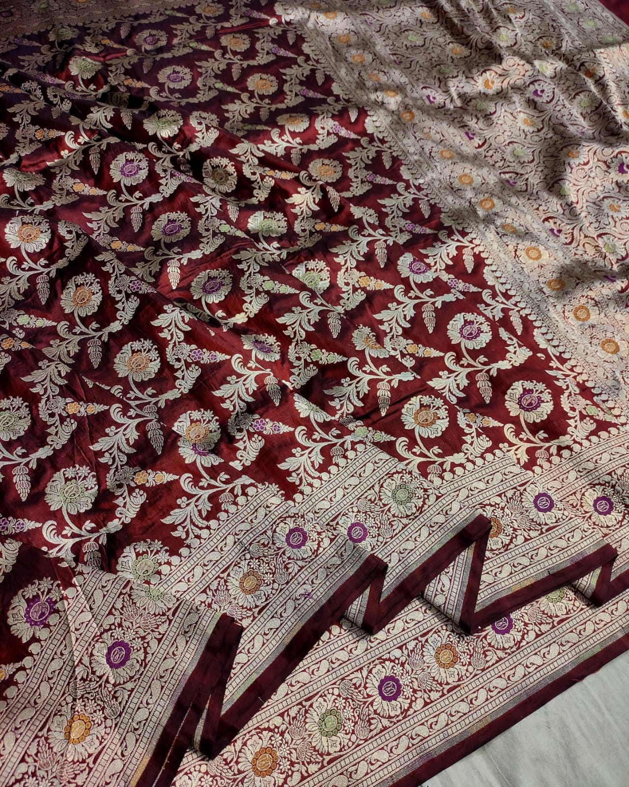 Close-up of a patterned fabric with intricate designs on a maroon and beige background.