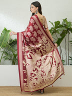 Woman wearing a maroon saree with gold patterns in a room with plants.