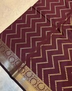 A close-up of a deep maroon or burgundy fabric with a repeating beige zigzag pattern and a decorative beige border with floral motifs.