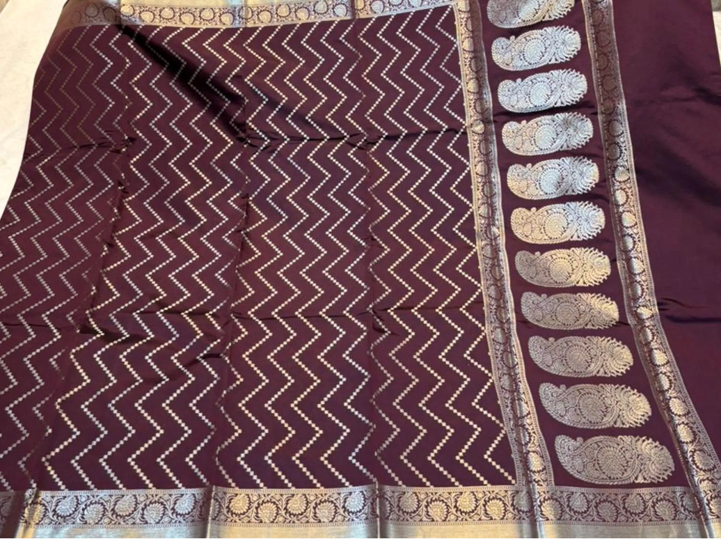 A deep maroon purple Banarasi silk saree with white zari ikat patterns and a wide silver border featuring detailed paisley motifs.