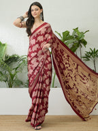 Woman wearing a maroon saree with elephant patterns against a white wall with plants.