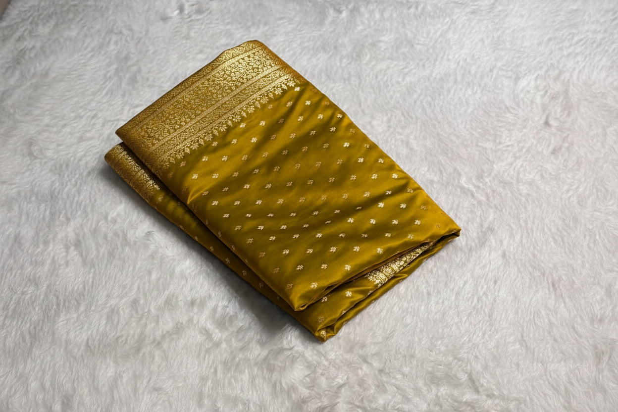 Green saree with gold border on a white textured surface with Zari brand box.