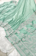 A mint green silk saree with a wide white border featuring floral and geometric patterns, draped over a white faux fur surface.