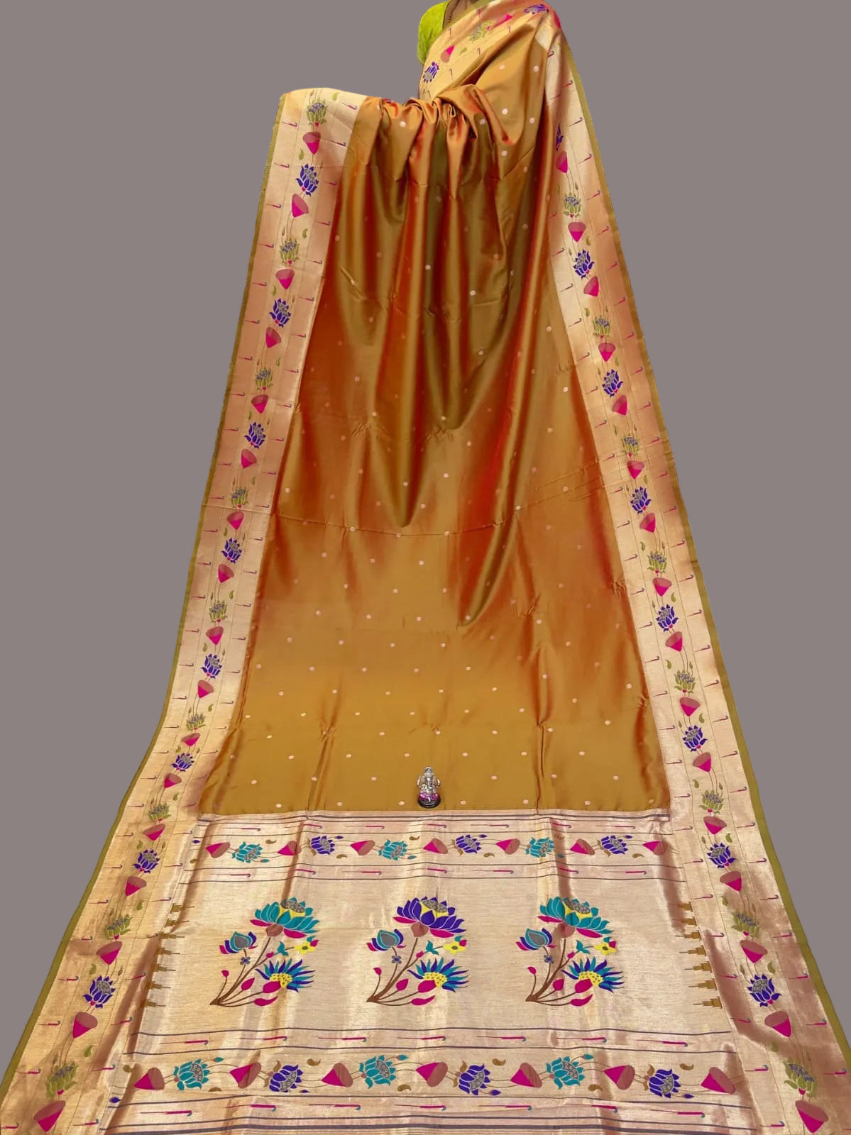 Orange saree with floral patterns on a white surface, with stacks of colorful sarees in the background.