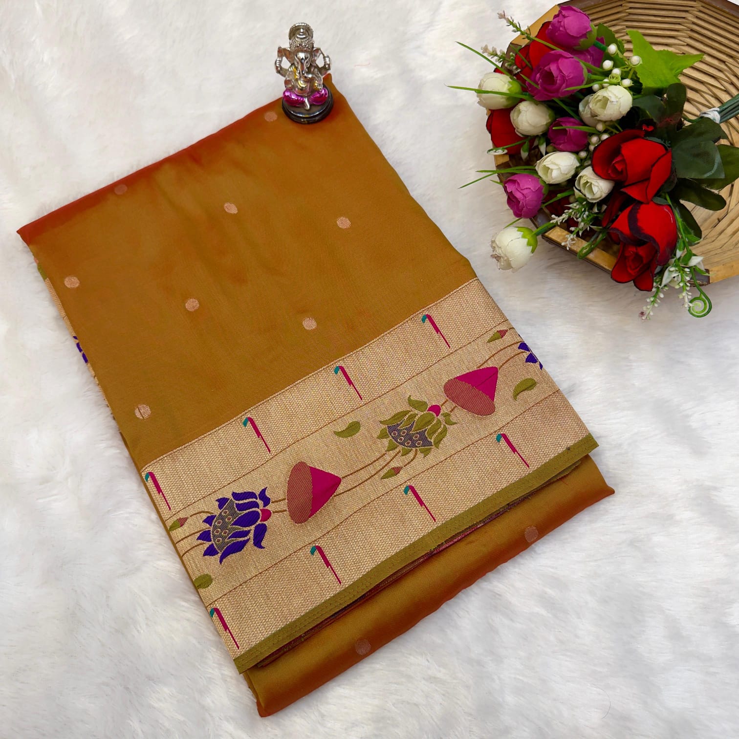 Brown saree with floral patterns on a white surface with flowers and a statue.