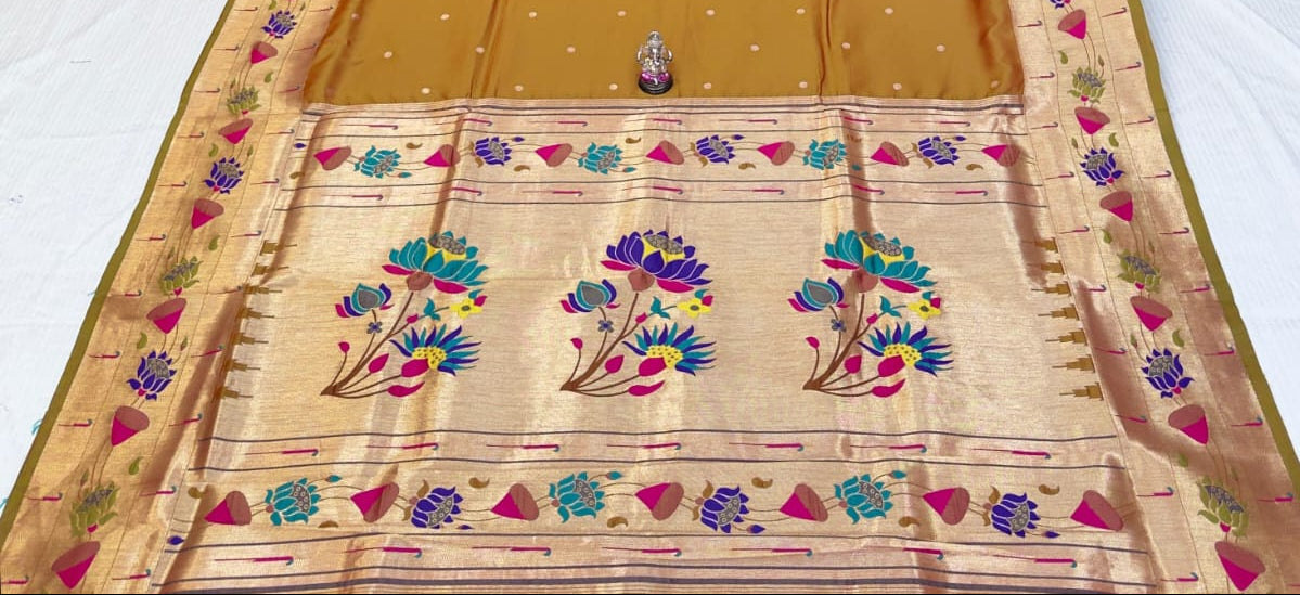 Orange saree with floral patterns on a white surface, with stacks of colorful sarees in the background.