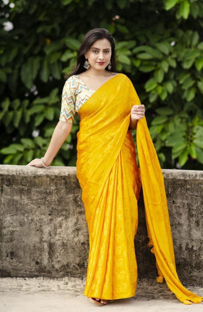 Woman in a yellow saree standing outdoors with greenery in the background