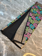 A folded black fabric garment, likely a saree or dupatta, displayed on a gray marble surface. The fabric features a prominent floral pattern in pink, green, and blue, with a wide beige and black patterned border.
