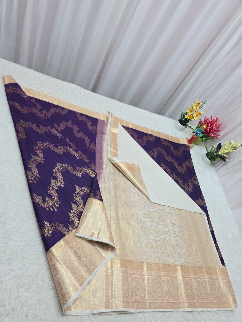 Purple and beige saree with floral decorations on a white table