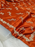 Orange fabric with gold embroidery on a white surface