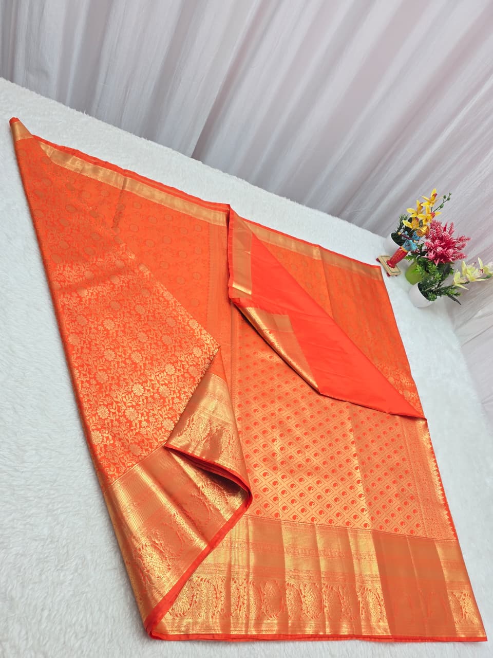Orange saree with a floral arrangement on a white surface