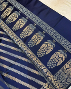 A close-up of a navy blue fabric textile with metallic gold block-printed motifs, including a border pattern and horizontal striped sections.