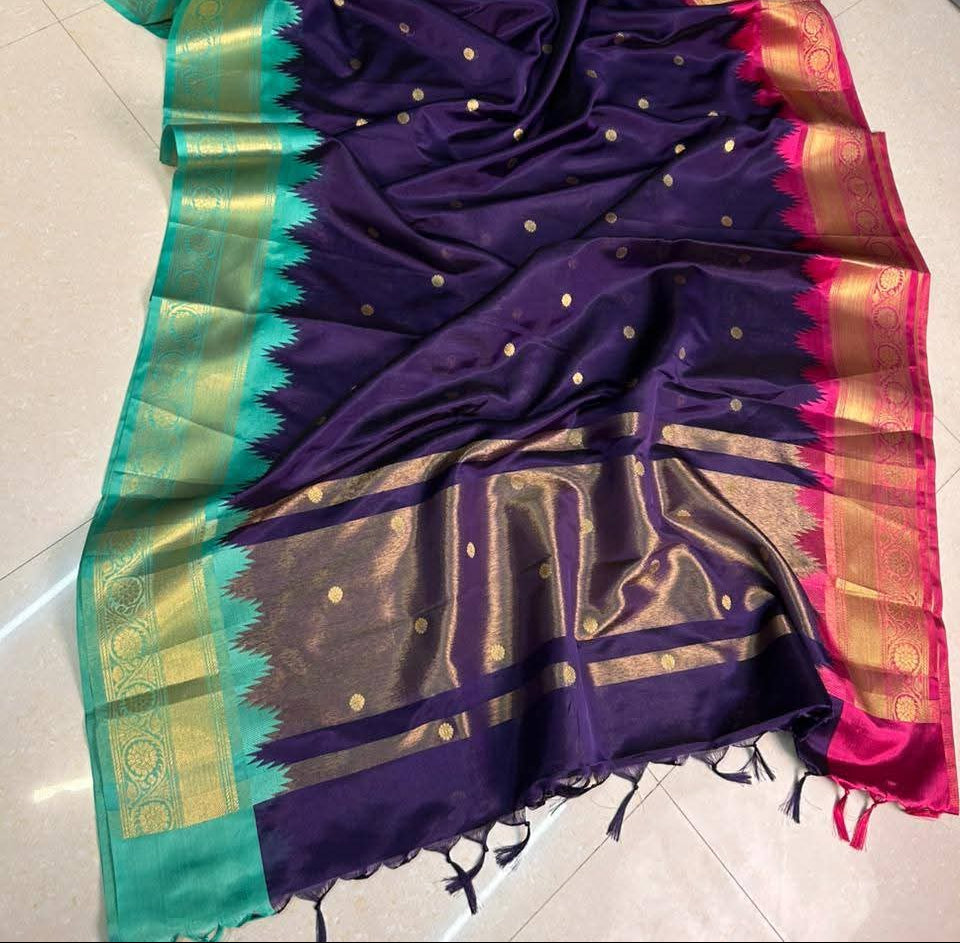 A purple silk saree with gold zari work, featuring a teal green border, a gold and pink border, and small gold dots scattered across the body.