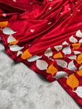 A close-up of a rich red silk saree with intricate silver and gold leaf embroidery, draped over a white faux fur surface.