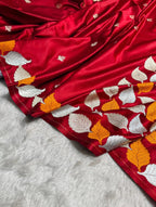 A close-up of a rich red silk saree with intricate silver and gold leaf embroidery, draped over a white faux fur surface.