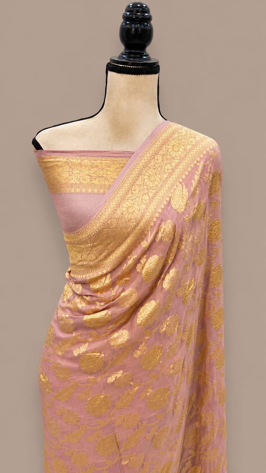 A pink and gold Banarasi silk saree draped on a mannequin torso, featuring intricate gold zari floral motifs and a matching pink blouse.