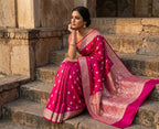 Woman in a pink saree sitting on stone steps with a historical building in the background
