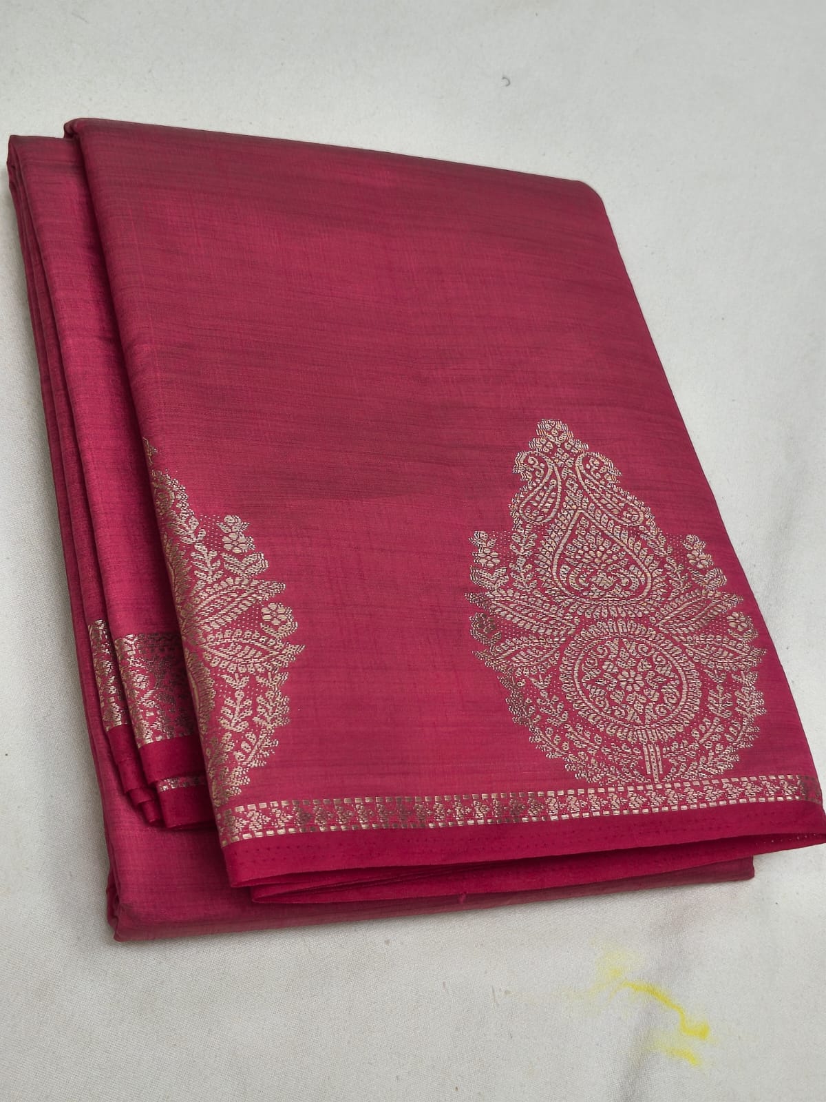 Folded pink saree with white floral patterns on a white background
