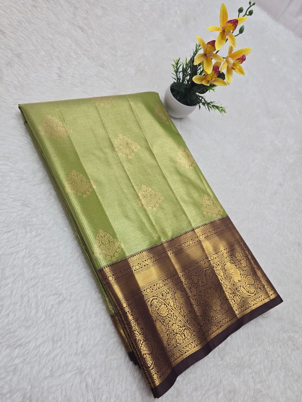 Green and brown saree with floral decoration on a white background