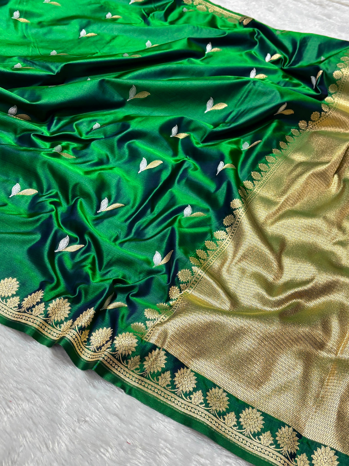 A green silk saree with gold zari embroidery, featuring small white floral motifs and a wide gold border.