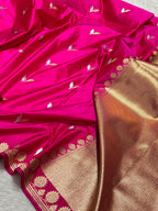 A close-up of a bright pink silk saree with small gold and white woven motifs, featuring a wide metallic gold border with floral zari embroidery.