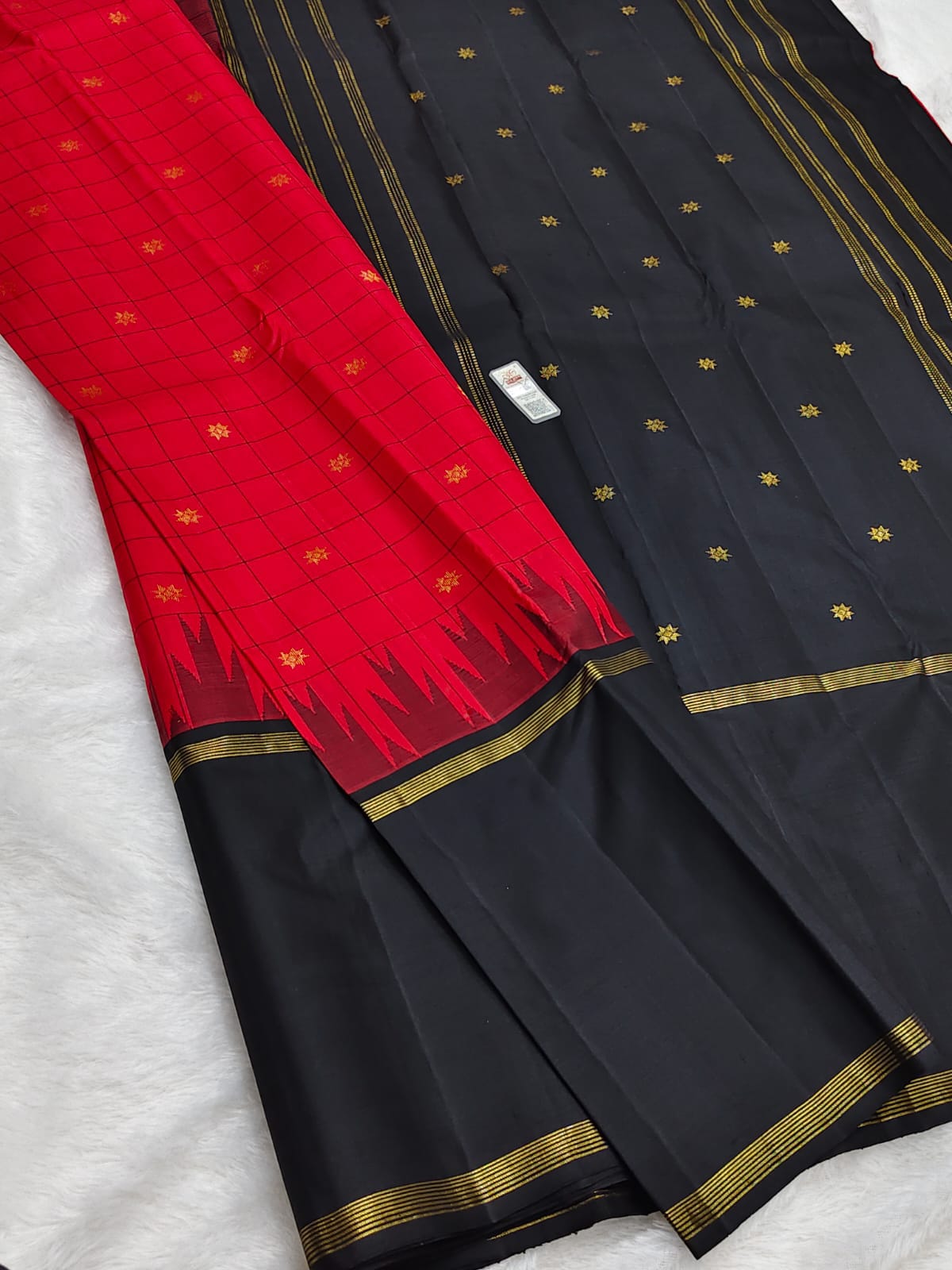 A black and red silk saree with gold zari borders and motifs, laid flat on a white textured surface.