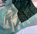 A dark green and light teal green Banarasi silk saree with gold zari woven motifs, held up by a person in a shop setting.