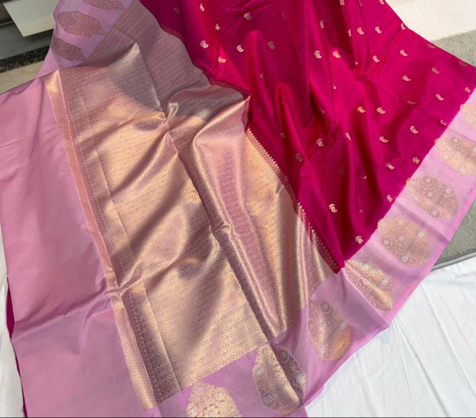 A pink and magenta silk saree with gold zari Banarasi motifs, held up by a person in a showroom.