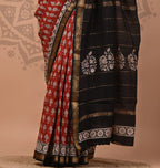 Woman wearing a red and black saree with white patterns on a beige background