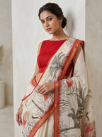 Woman wearing a red blouse and white saree with floral patterns against a plain background