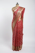 Red saree with white floral patterns and gold border on a green surface