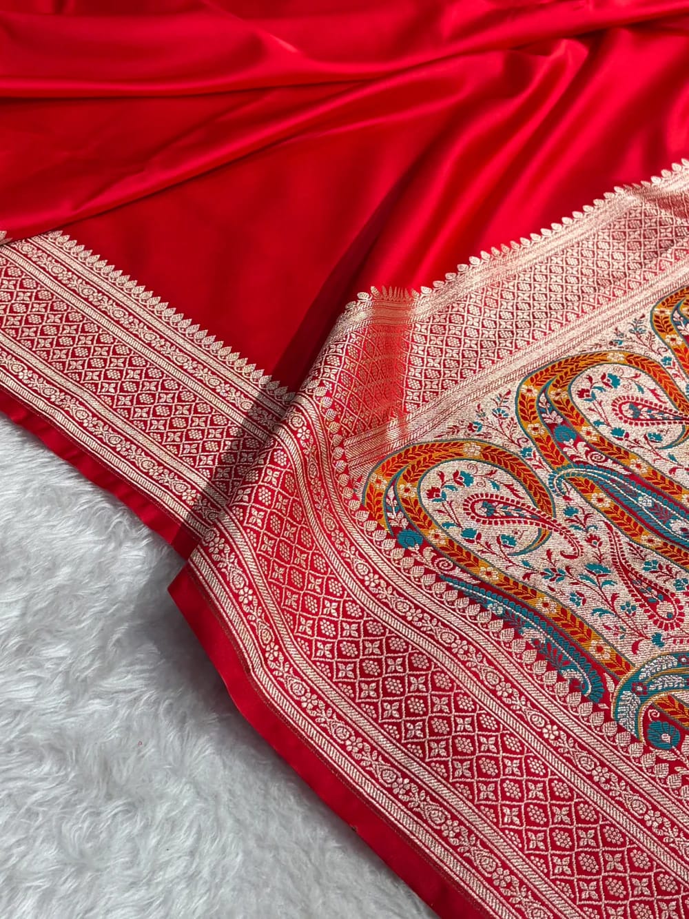 Red fabric with intricate white and multicolor patterns on a white background