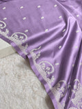 A close-up of a lavender purple fabric, likely a saree or dupatta, featuring intricate silver floral embroidery along the border and scattered small motifs.