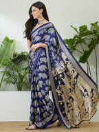 Woman wearing a blue saree with elephant patterns against a white wall with green plants.