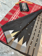 A black and red Banarasi silk saree with intricate gold, silver, and white zari embroidery, displayed on a gray marble floor with a folded black dupatta and wooden hanger.