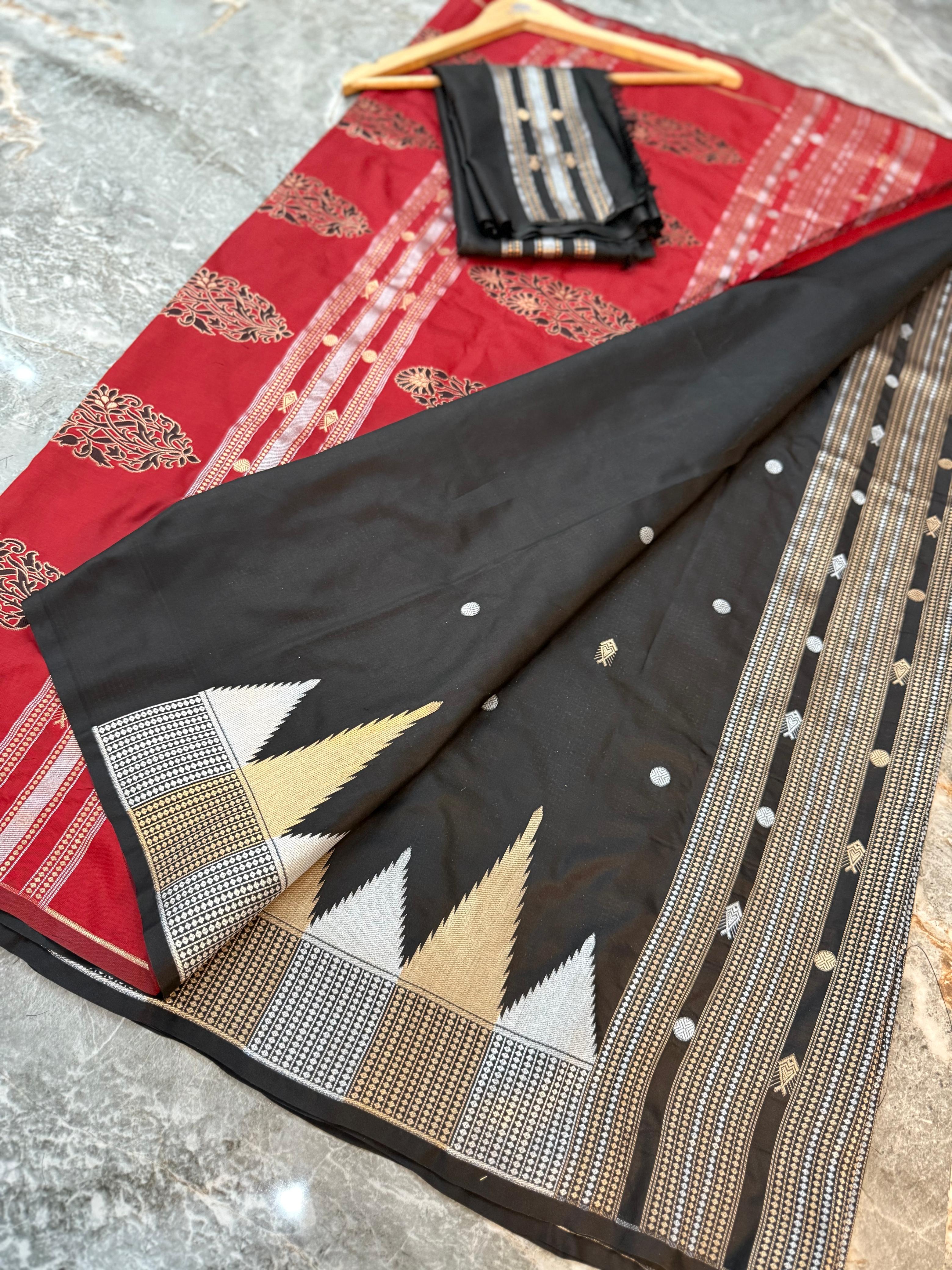 A black and red Banarasi silk saree with intricate gold, silver, and white zari embroidery, displayed on a gray marble floor with a folded black dupatta and wooden hanger.