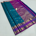A teal blue and purple silk saree with intricate gold zari woven patterns and borders, displayed diagonally on a light gray background.