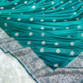 Teal fabric with white floral patterns and intricate silver border on a white background