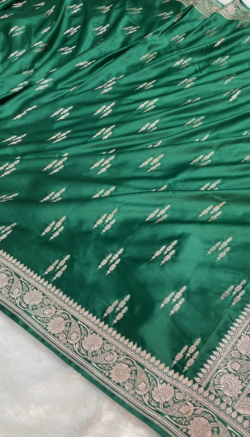 A close-up of a green Banarasi silk saree with intricate silver zari embroidery and a detailed floral border.