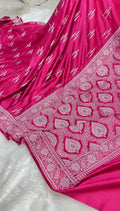 A close-up of a bright pink fabric garment, likely a sari or dress, featuring intricate silver paisley and floral border embroidery and small silver motifs throughout.
