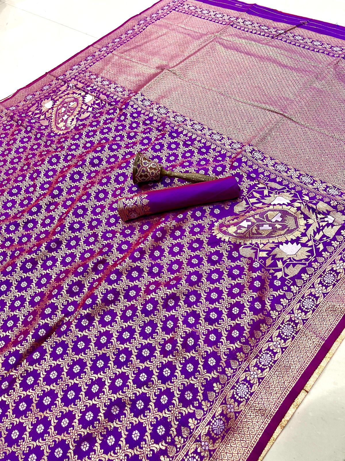 Purple and pink saree with intricate patterns and a decorative item on a white background