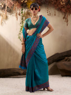 Woman in a teal saree with a red border standing against a neutral background