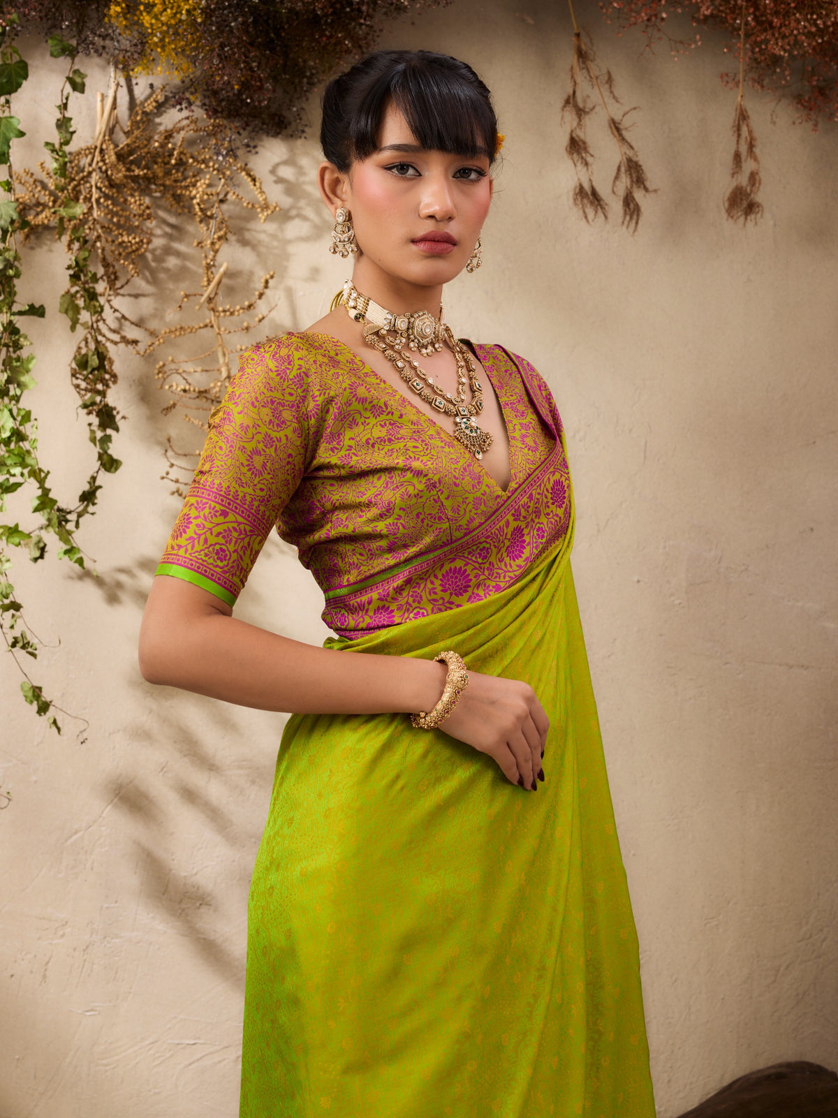Woman wearing a green saree with a pink blouse against a neutral background