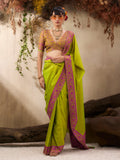 Woman wearing a green saree with pink border against a natural background