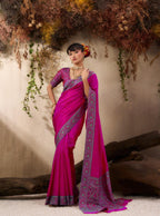 Woman in a pink saree with intricate patterns standing against a natural backdrop.