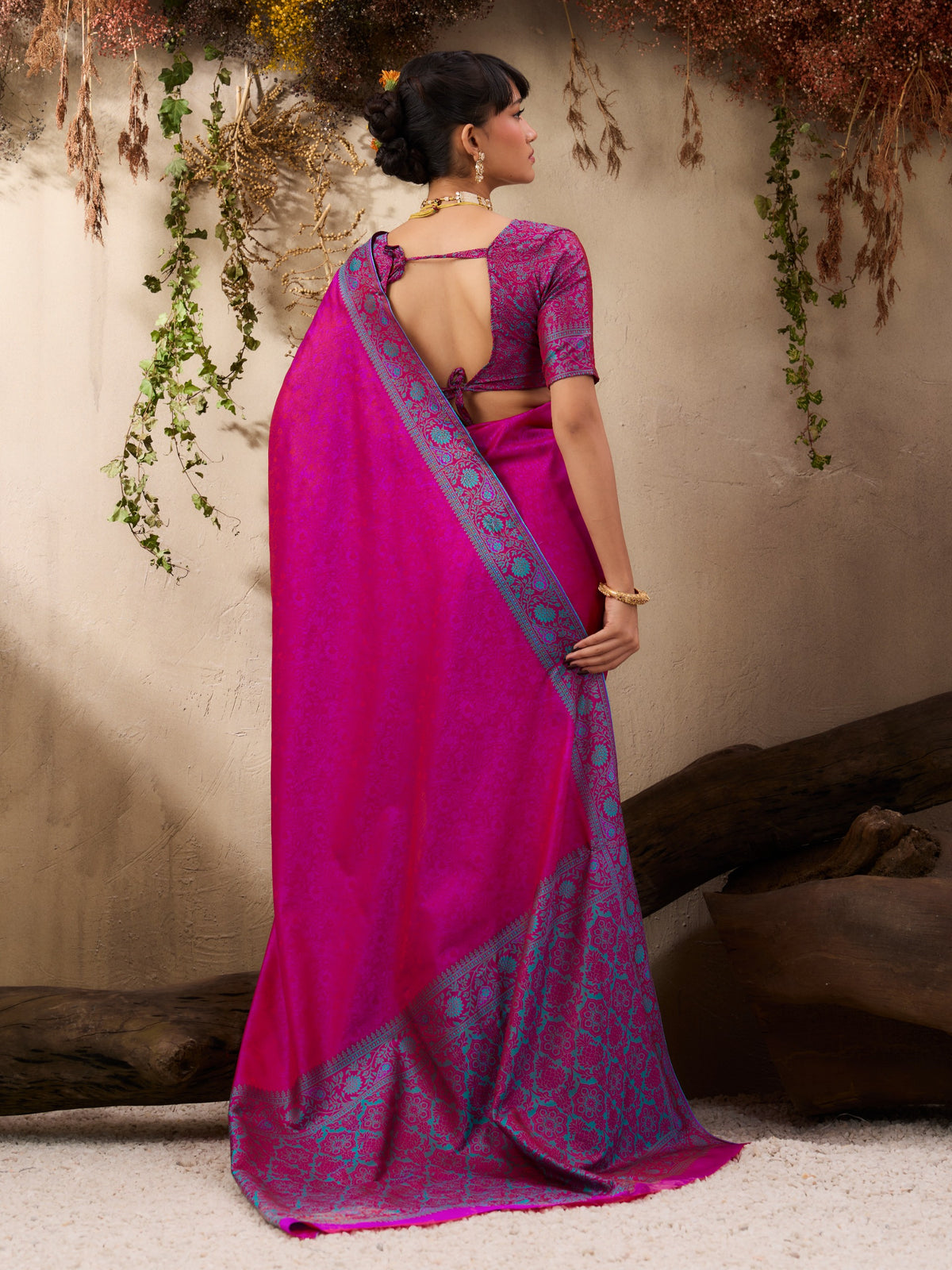 Woman wearing a pink saree with a blue blouse against a neutral background